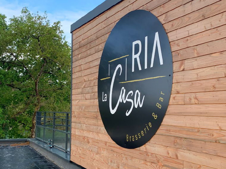Gros plan de l’enseigne ronde du restaurant La Casa Ria sur la façade en bois