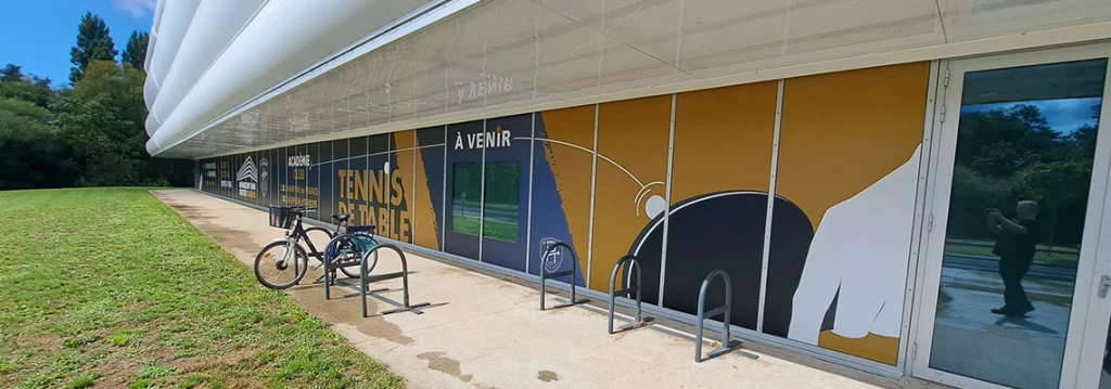 Vue côté droit des baies vitrées du Hennebont Ping Center avec illustrations vectorielles de mains jouant au tennis de table sur fond noir